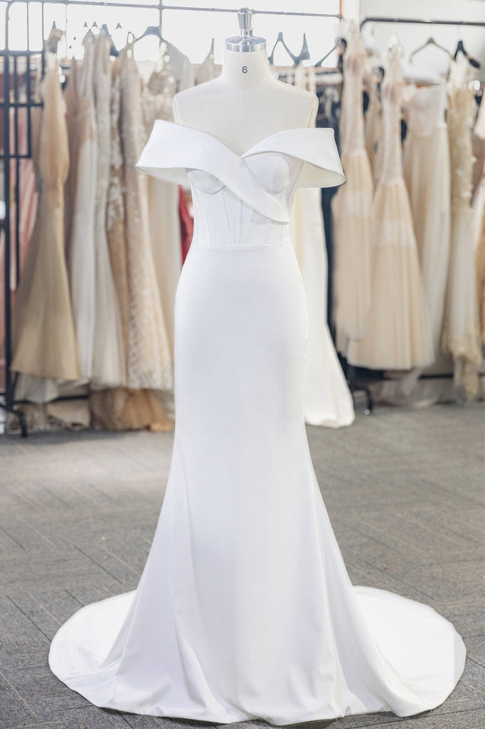 A stunning wedding dress with an off-the-shoulder neckline, made of smooth crepe fabric with a corset bodice and a flared skirt that hugs the waist and hips before flowing out into a beautiful silhouette.
